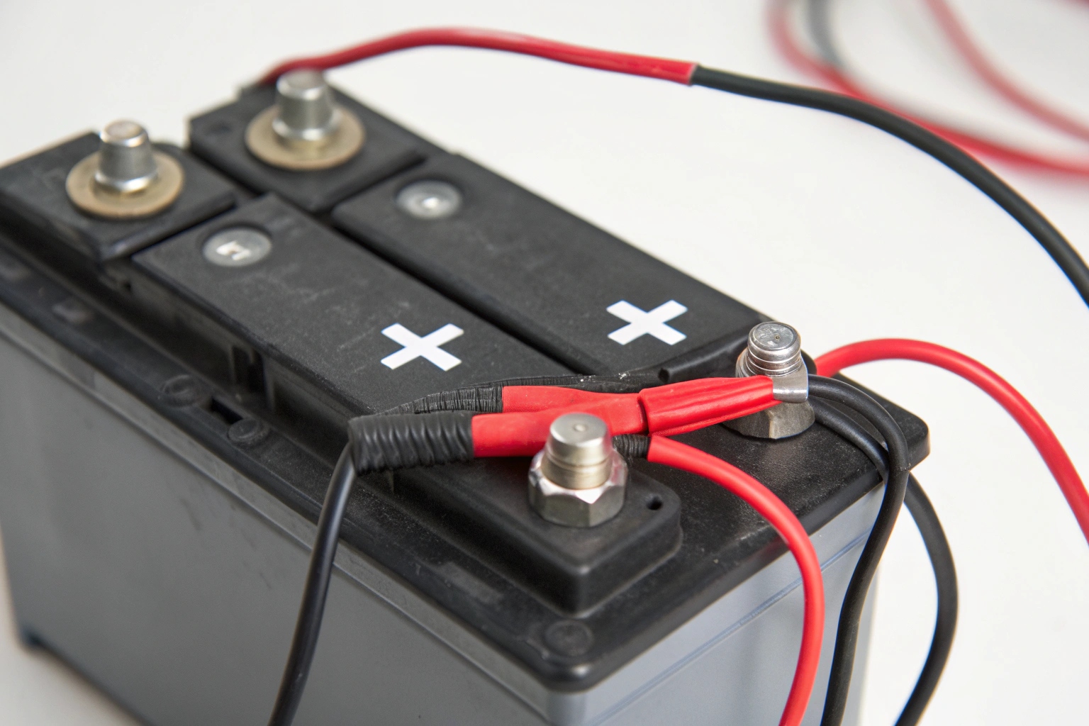 A close-up of a scooter battery showing red positive and black negative terminals