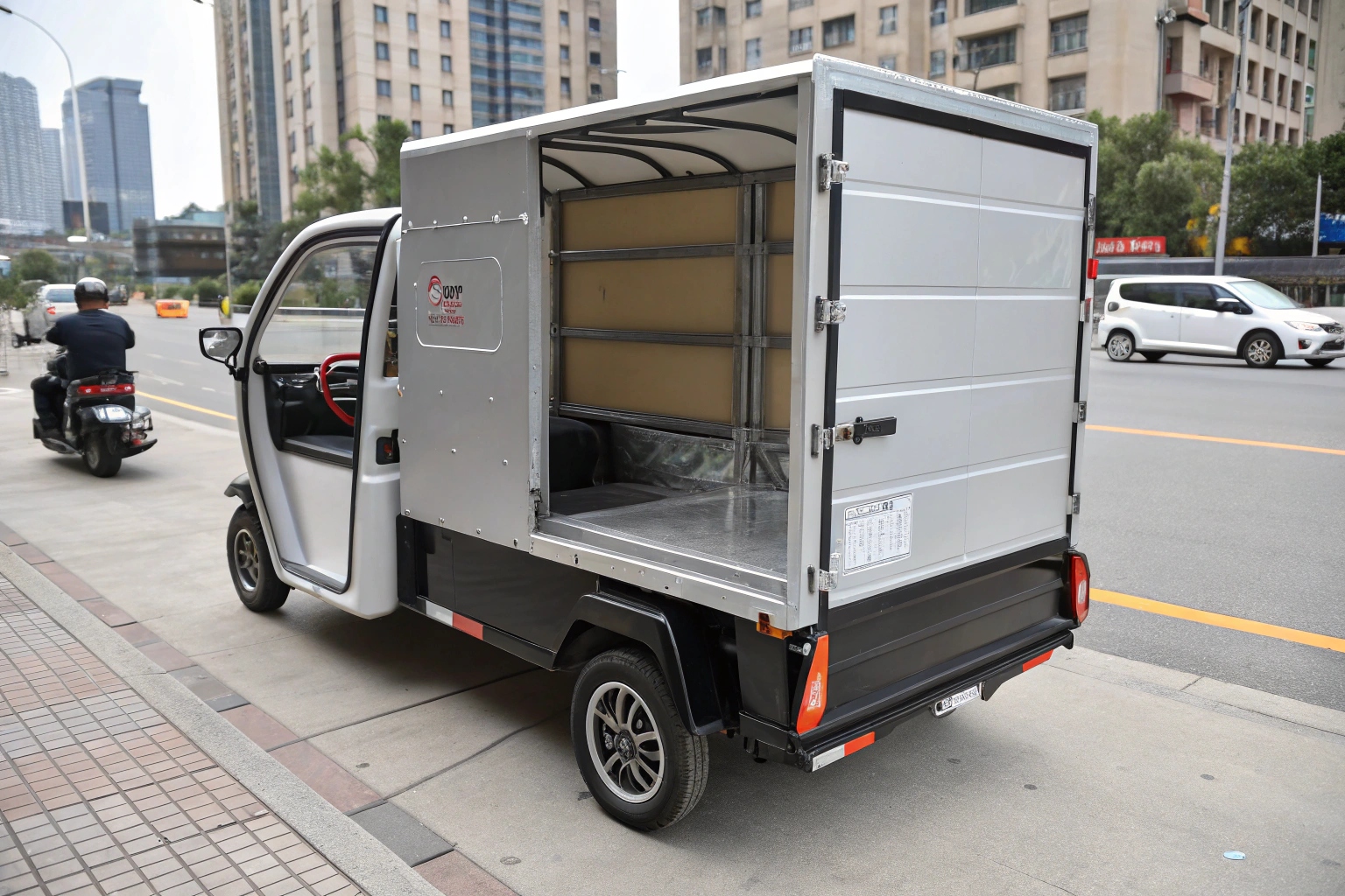 An electric delivery tuk tuk easily navigating a narrow street while a larger van is stuck behind