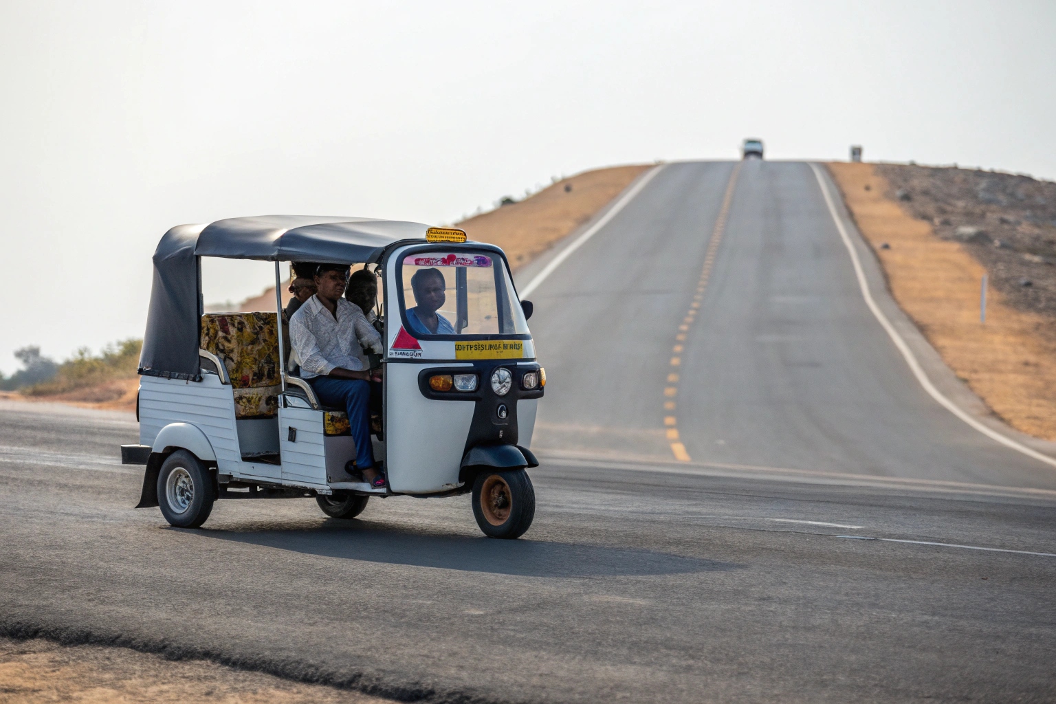 An electric tuk-tuk with passengers driving up a slight incline