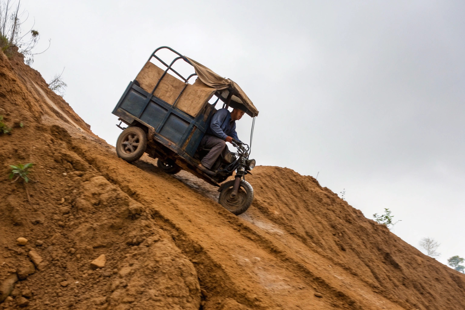 An electric tricycle effortlessly climbing a steep dirt hill with a full load